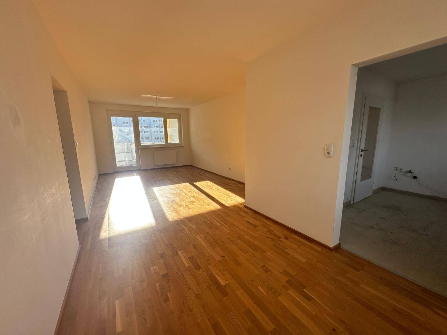 Geräumiges, helles Zimmer mit Holzboden und offener Verbindung zu weiteren Bereichen.