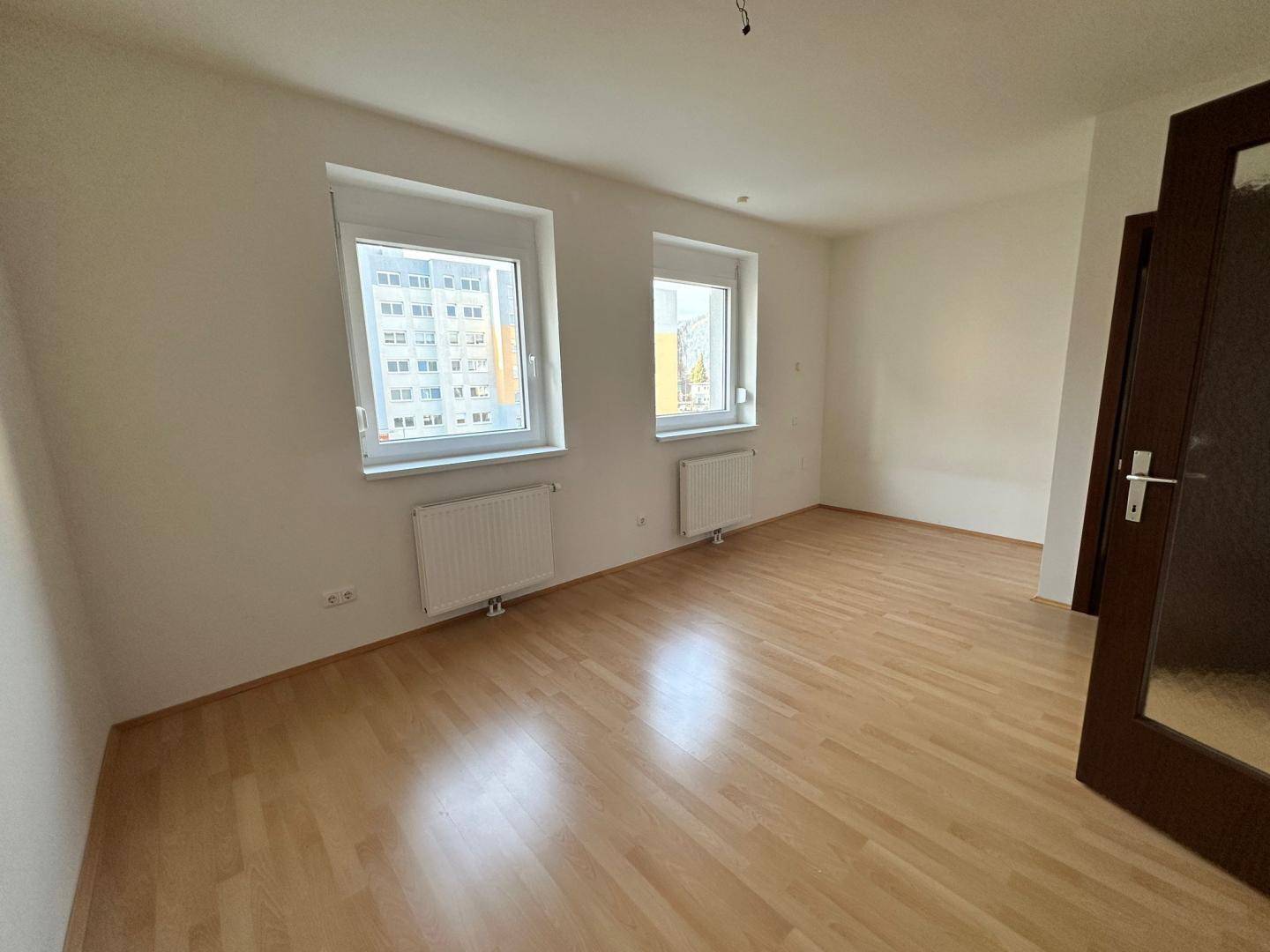 Helles Zimmer mit zwei Fenstern, Laminatboden und Blick auf die Nachbargebäude, vielseitig nutzbar.