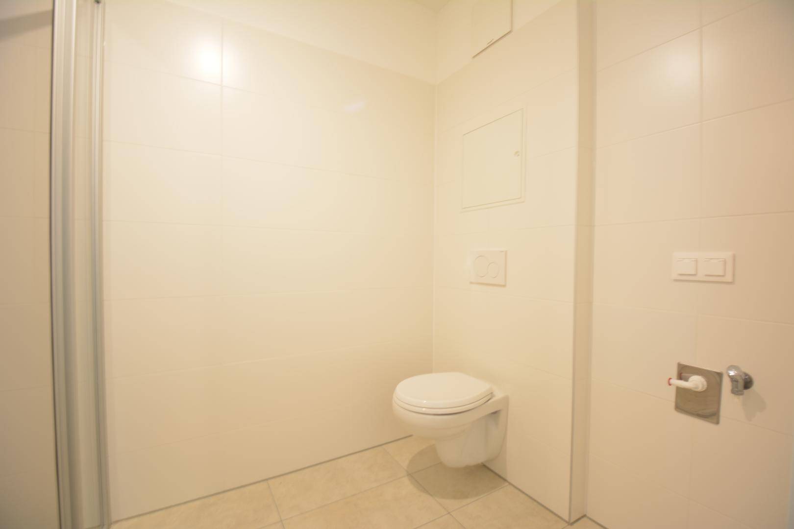 Modernes Badezimmer mit wandhängendem WC und Duschbereich, komplett gefliest in hellen Tönen.