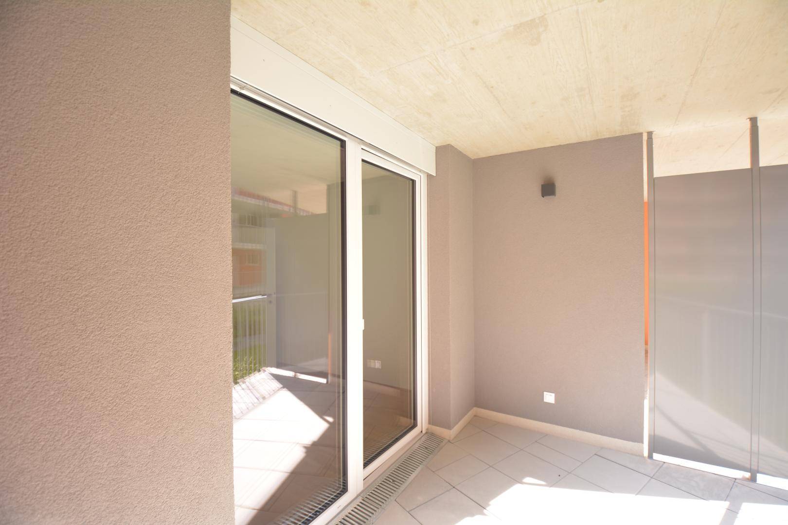 Heller Balkon mit Fliesenboden und großen Glasschiebetüren, die viel Licht hereinlassen.