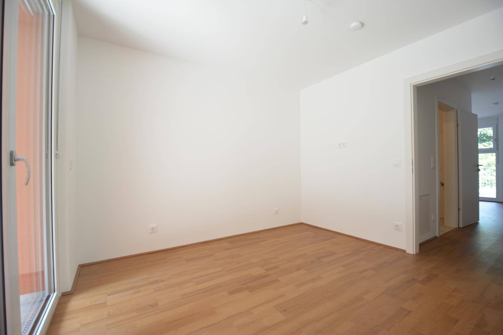 Heller Wohnraum mit Holzfußboden und Zugang zu einem Balkon, ideal für natürliche Belichtung.