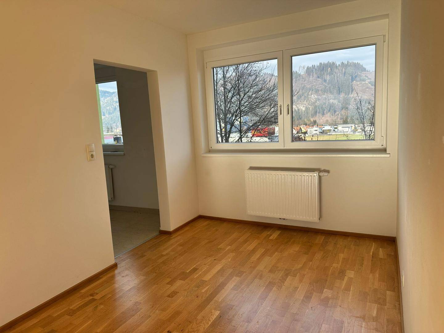 Geräumiges Zimmer mit Holzboden, großem Fenster und schöner Aussicht auf die Berge.