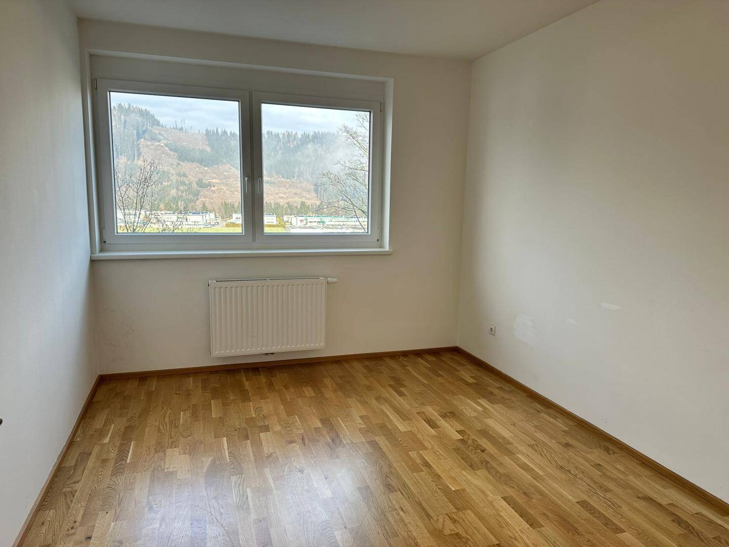 Helles Zimmer mit Parkettboden und weitem Blick auf die grüne Berglandschaft.