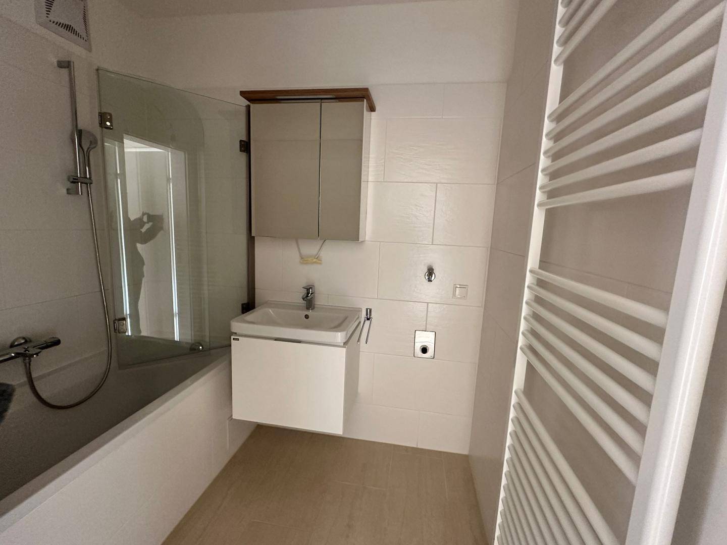 Modernes Badezimmer mit Badewanne, Duschwand, Waschbecken und beheiztem Handtuchhalter.