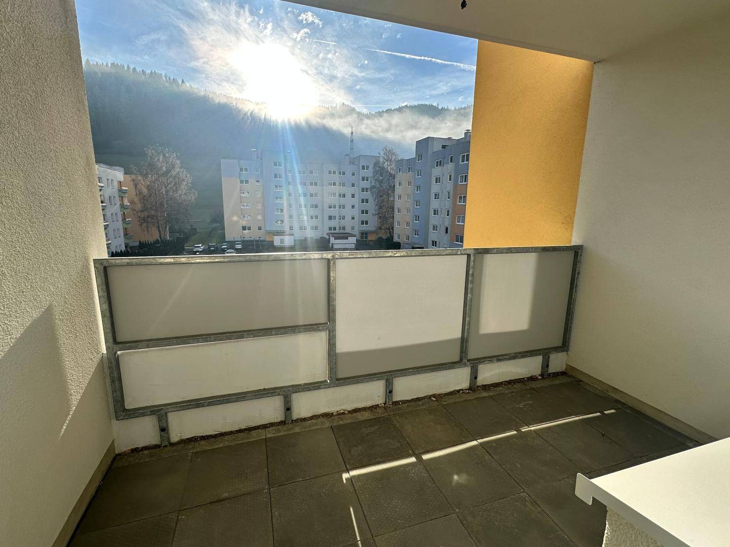 Sonniger Balkon mit Fliesenboden und Panoramablick auf die Berge und umliegende Bebauung.