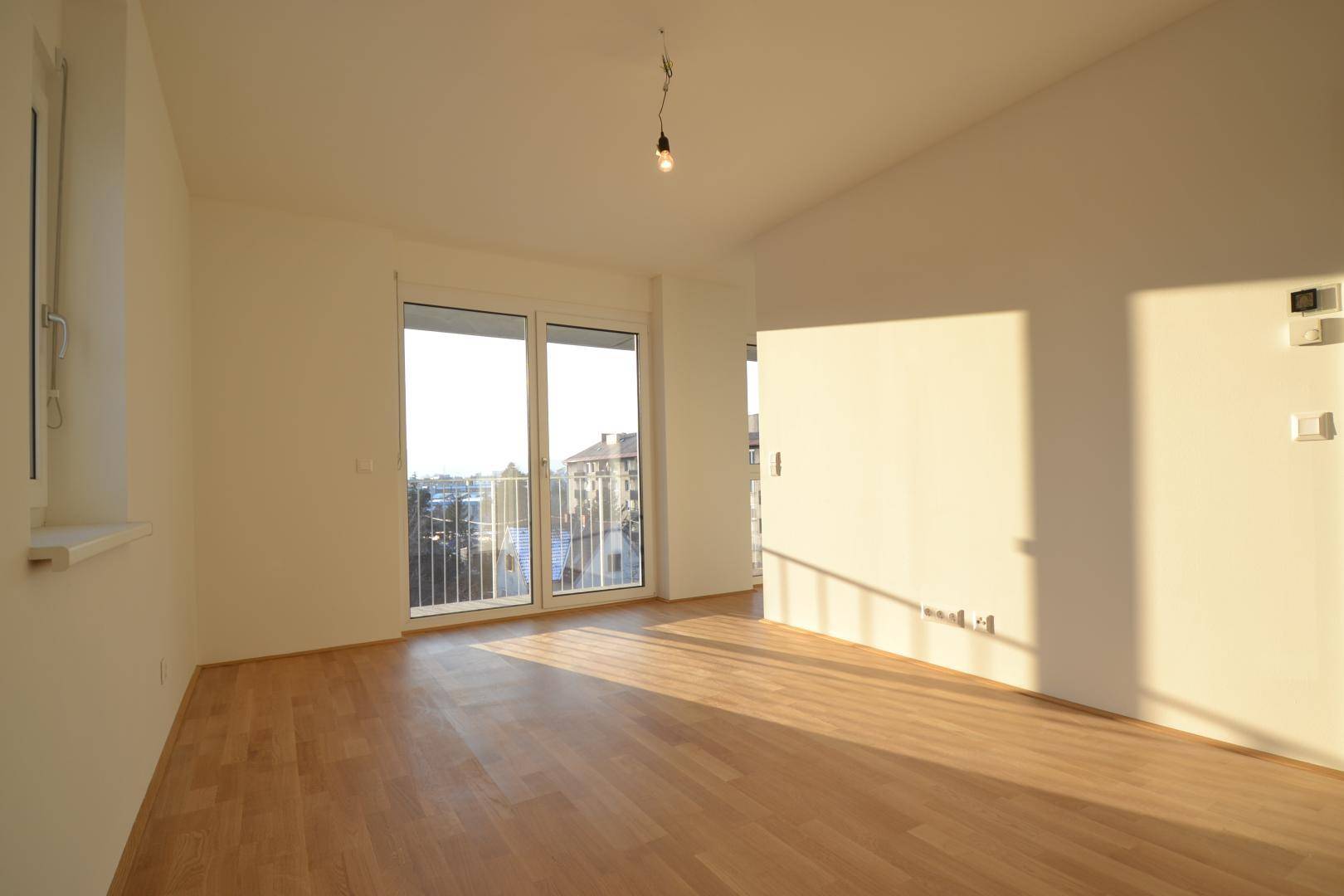 Lichtdurchfluteter Raum mit Parkettboden und Zugang zu einem Balkon, bietet einen weiten Blick.