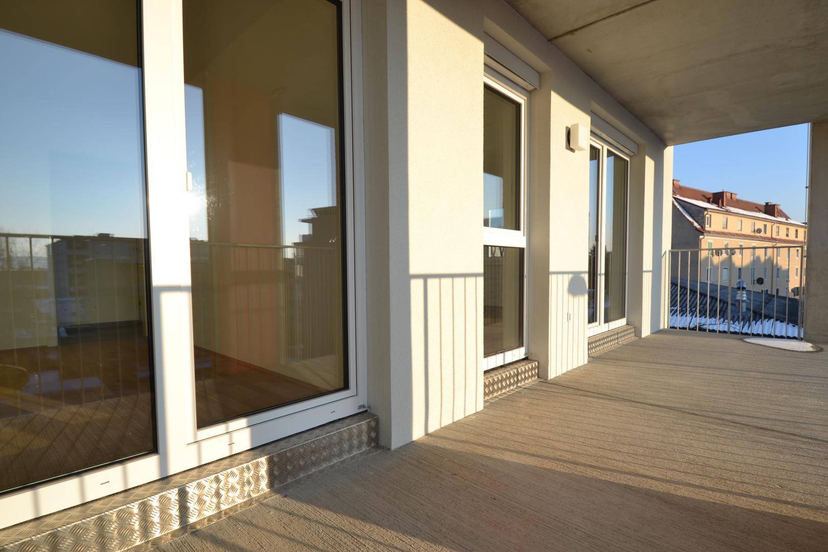 Breiter Balkon mit großen Fenstern und Türen, die viel Licht in die Innenräume lassen.