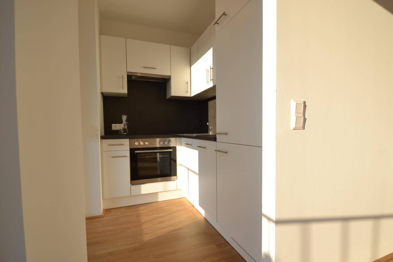 Moderne Einbauküche mit weißen Schränken, dunkler Arbeitsplatte und integriertem Backofen.