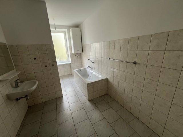 Badezimmer mit beigefarbenen Fliesen, Badewanne, Waschbecken und einem Fenster für Tageslicht.