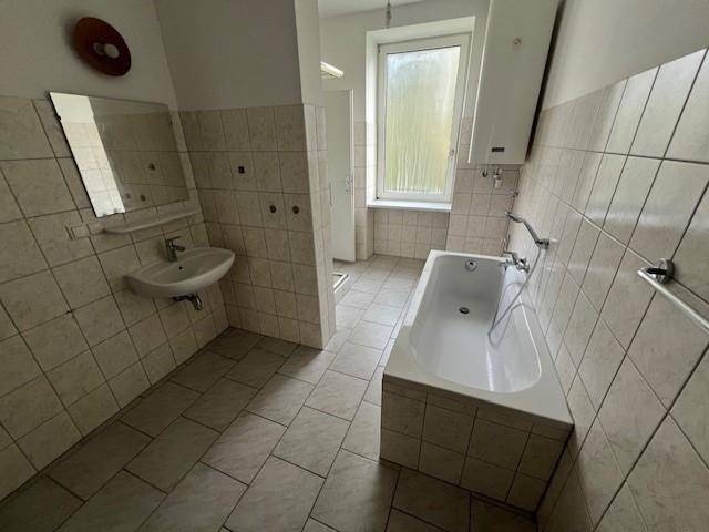 Funktionales Badezimmer mit Badewanne, Waschbecken und hellen Fliesen, ausgestattet mit einem Fenster.