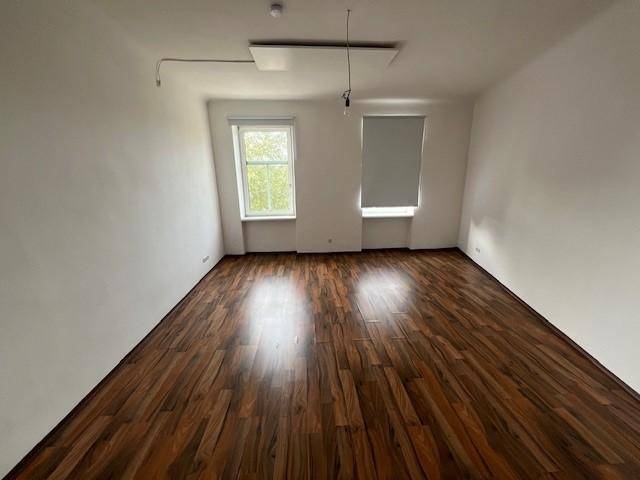 Helles Zimmer mit zwei Fenstern, Laminatboden und weißen Wänden, bietet viel Tageslicht.