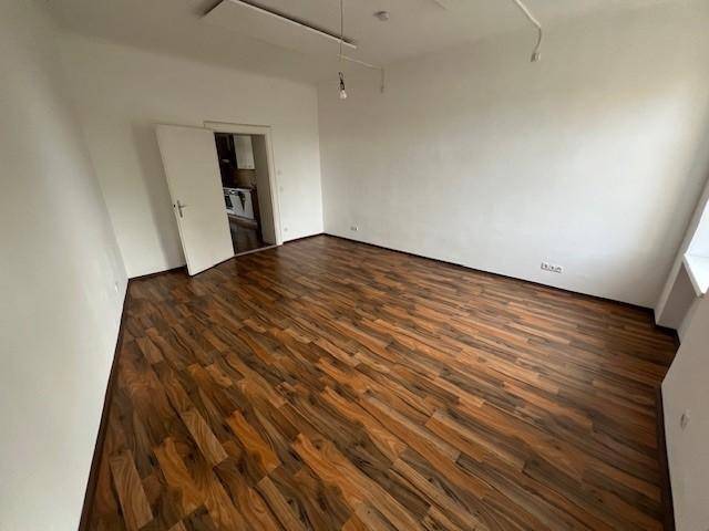 Geräumiges, leeres Zimmer mit hellem Laminatboden und weiß gestrichenen Wänden, bereit zum Einzug.