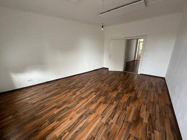 Helles und geräumiges Zimmer mit Laminatboden und weiß gestrichenen Wänden, ideal als Wohnbereich.