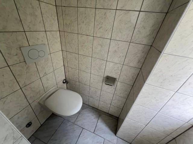 Separate Toilette mit Wand-WC und hellen Fliesen an Wänden und Boden.
