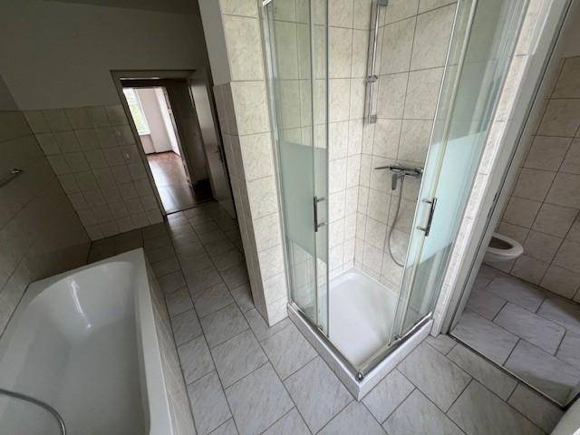 Badezimmer mit Duschkabine und separatem WC-Bereich, komplett gefliest in hellem Beige.