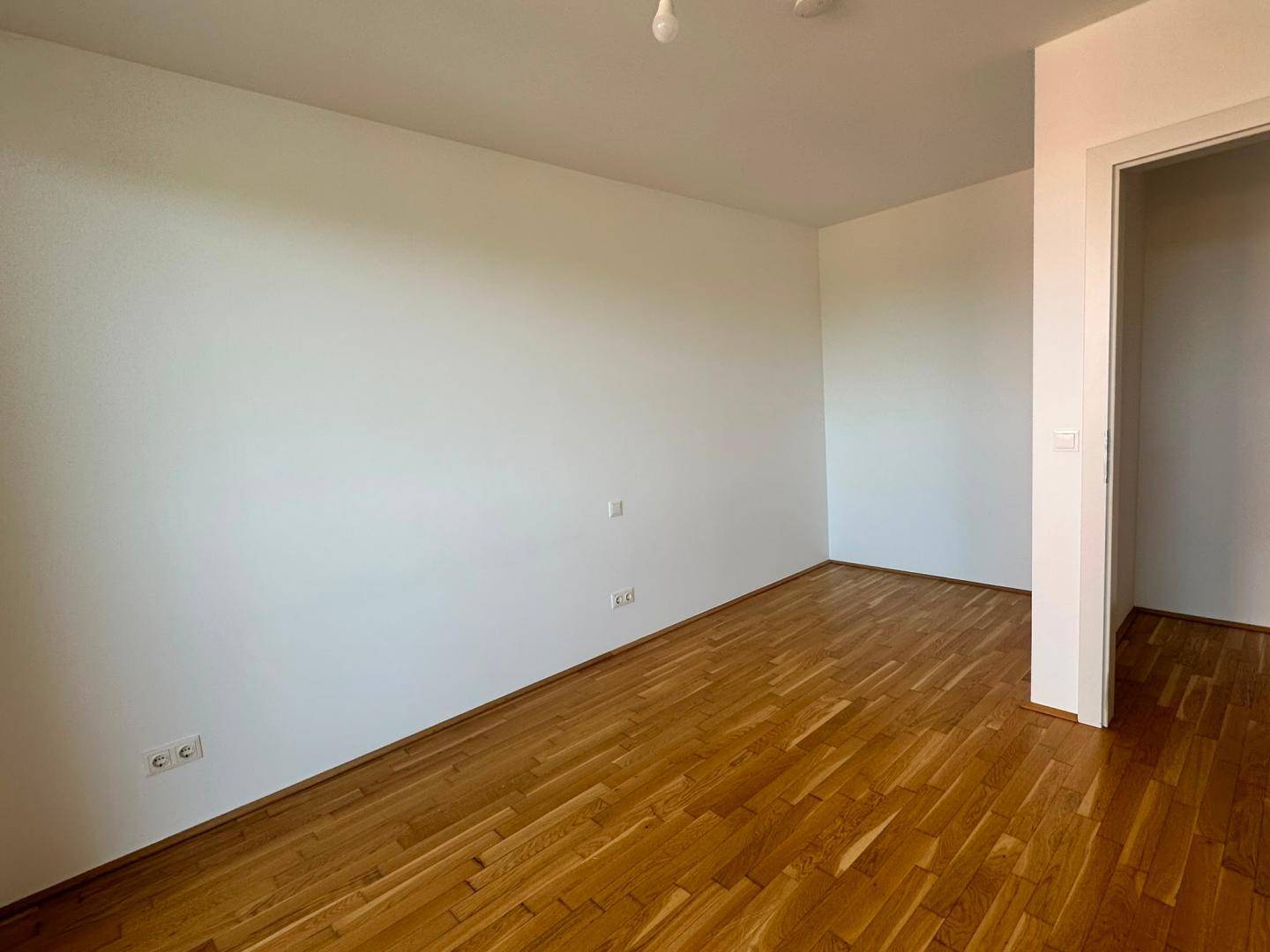 Leerer Raum mit hellem Parkettboden und weißen Wänden, ideal für verschiedene Nutzungsmöglichkeiten.