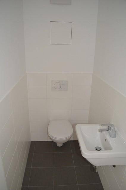 Modernes Gäste-WC mit wandhängendem WC, kleinem Waschbecken und grauen Bodenfliesen.