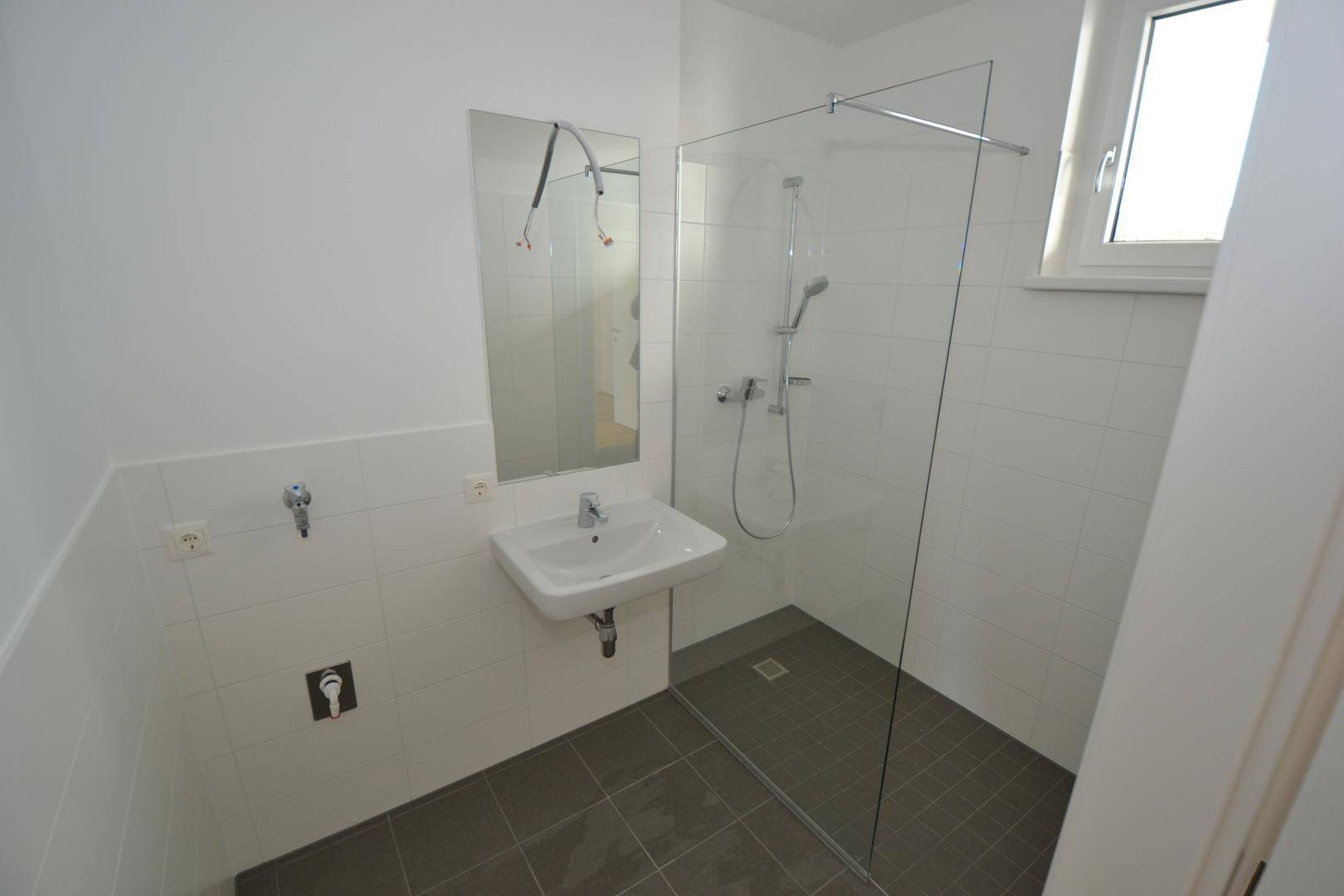 Modernes Badezimmer mit ebenerdiger Dusche, Waschbecken, Spiegel und Fenster für Tageslicht.