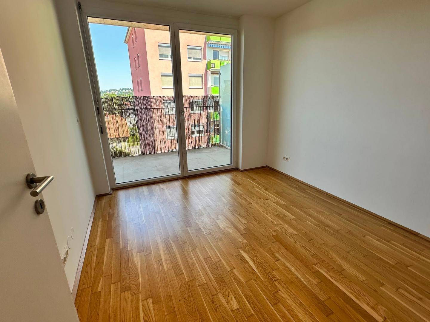 Helles Schlafzimmer mit Parkettboden und Balkonzugang, bietet einen Blick auf die Umgebung.