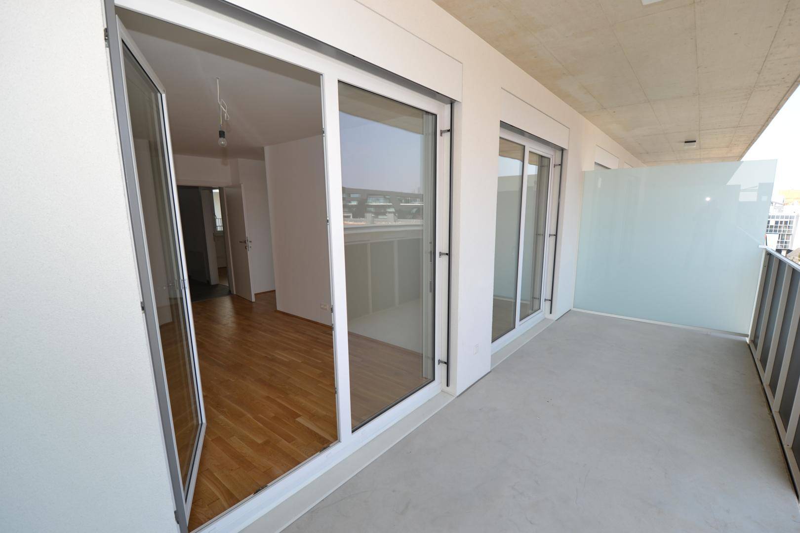Langer Balkon mit Betonboden und mehreren Zugängen zu den Innenräumen der Wohnung.