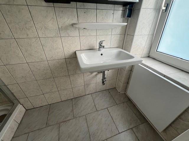 Badezimmer mit Waschbecken, Fenster und hellen Fliesen an Wänden und Boden.
