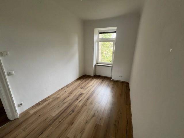 Leeres Zimmer mit Laminatboden und weiß gestrichenen Wänden, bereit zur individuellen Gestaltung.