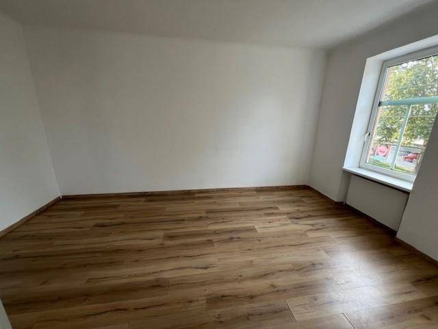 Geräumiges, leeres Zimmer mit Laminatboden und einem Fenster, das einen Blick nach draußen bietet.