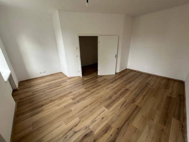 Leeres Zimmer mit Laminatboden und weiß gestrichenen Wänden, bereit zur individuellen Einrichtung.