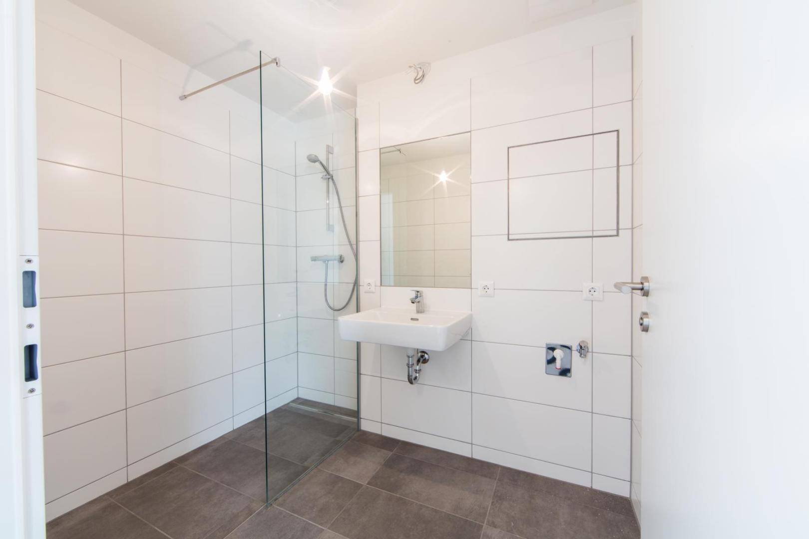 Modernes Badezimmer mit weißen Fliesen, ebenerdiger Dusche und einem einzelnen Waschbecken.