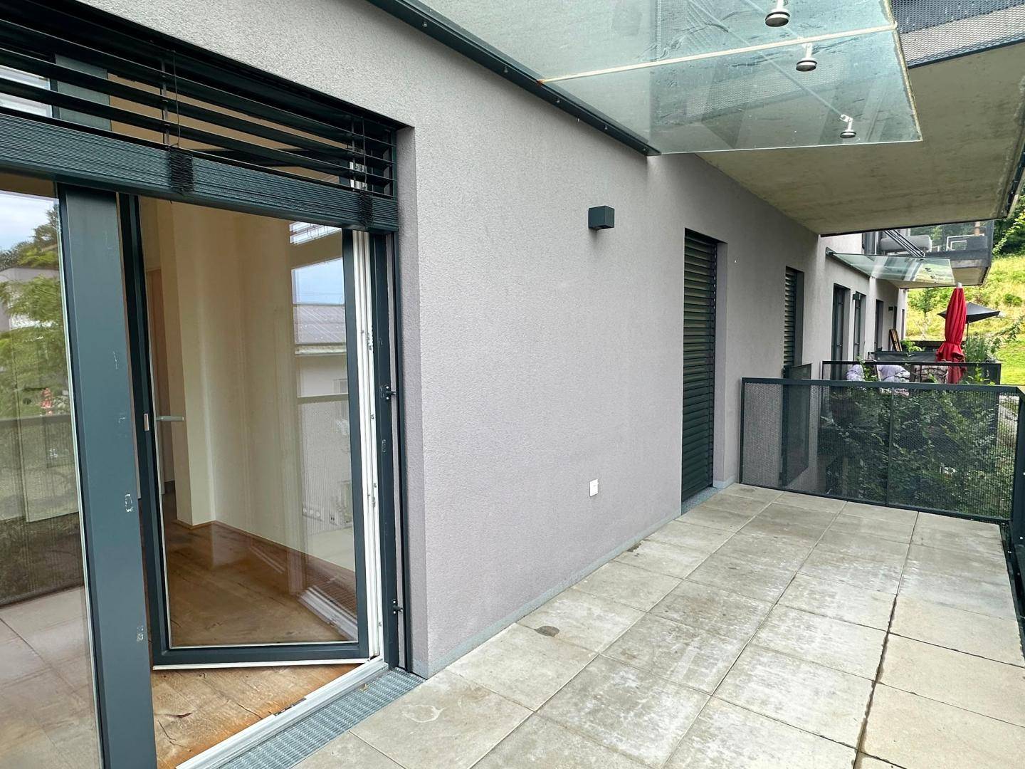 Moderner Balkon mit Fliesenboden und Glasüberdachung, bietet Zugang zum Innenbereich.