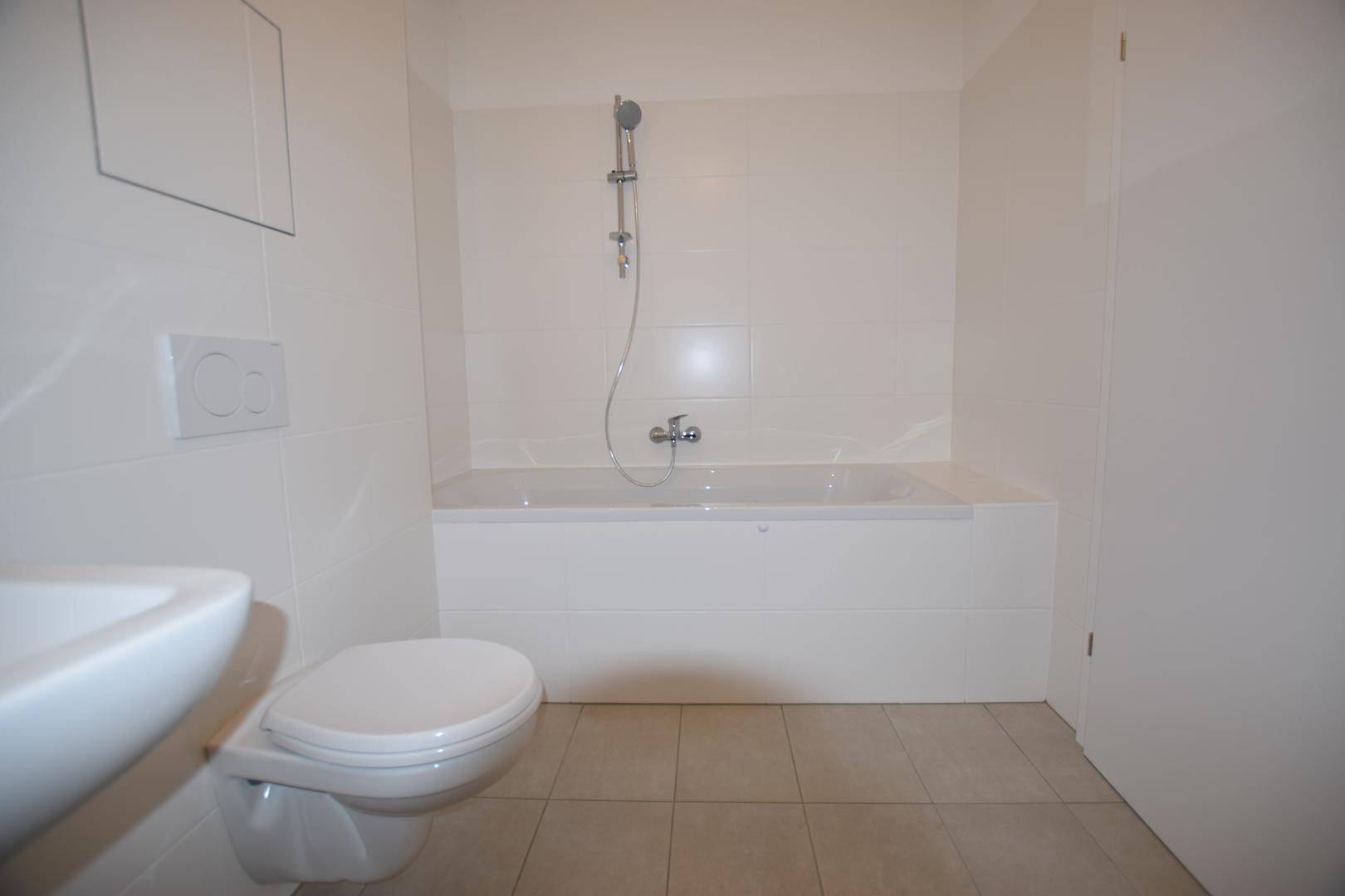 Modernes Badezimmer mit weißen Fliesen, Badewanne mit Duschfunktion, Toilette und Waschbecken.