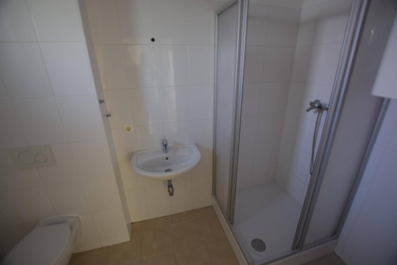 Modern gefliestes Badezimmer mit Duschkabine, Waschbecken und WC, in hellen Farbtönen gehalten.