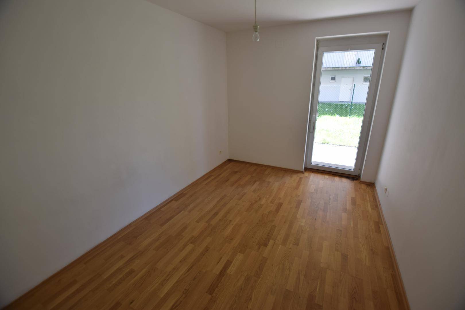 Helles Zimmer mit Parkettboden und direktem Zugang zur Grünfläche, ideal als Schlaf- oder Arbeitszimmer.