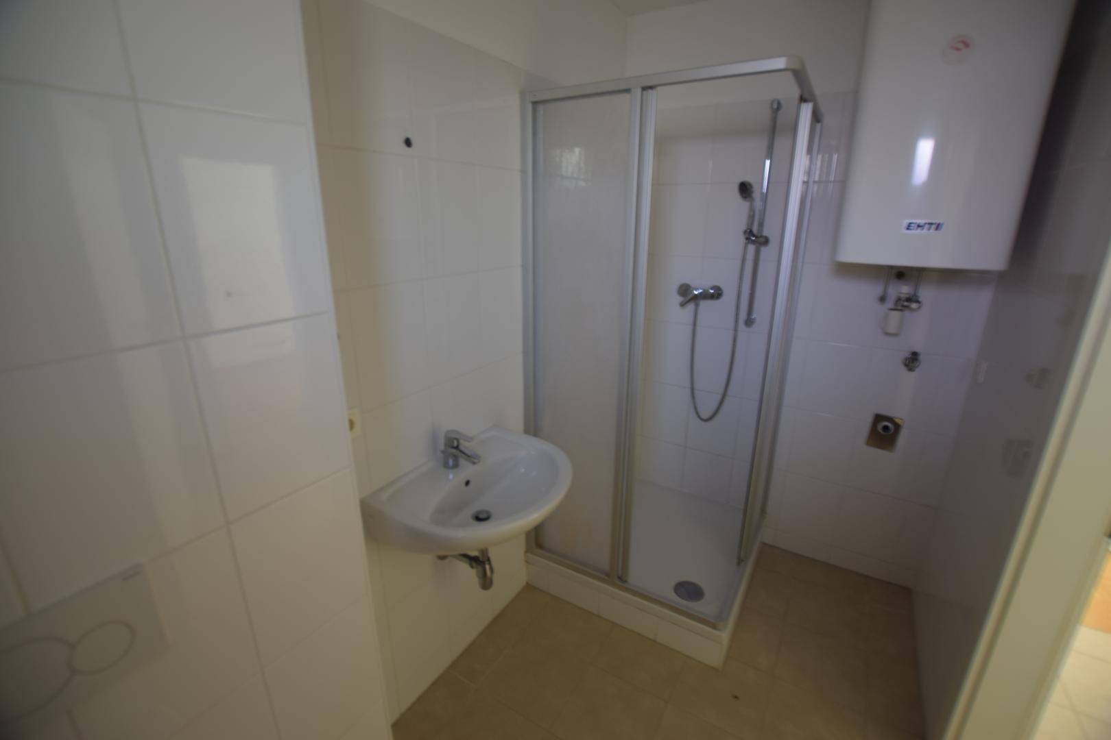 Praktisches Badezimmer mit Duschkabine, Waschbecken und Wandboiler, komplett gefliest.