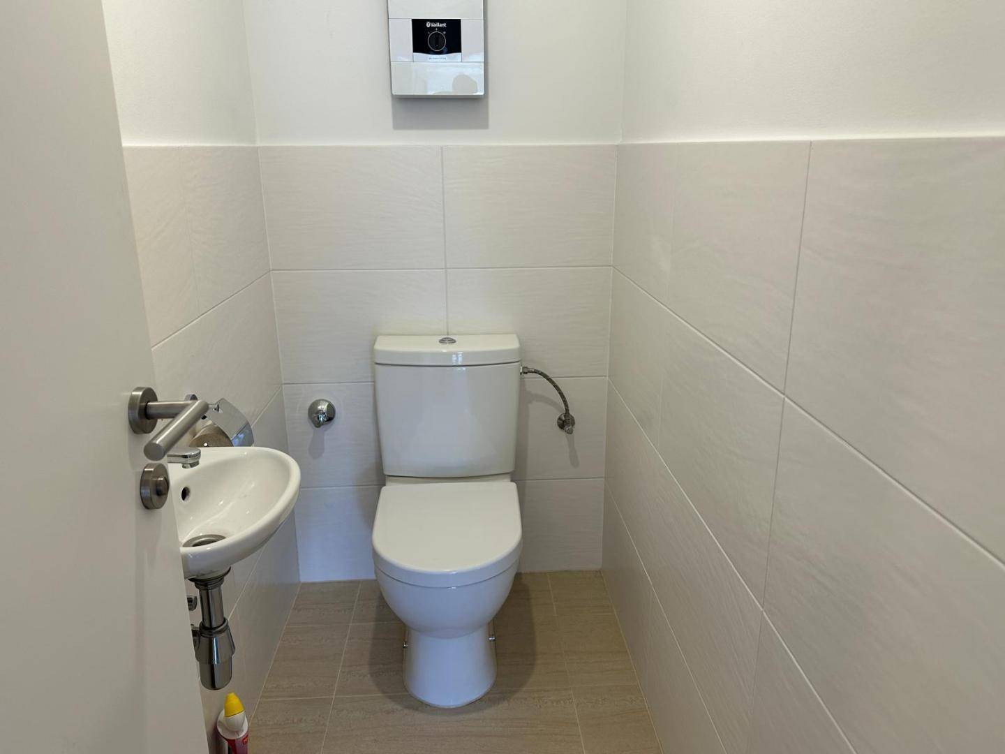 Modernes Gäste-WC mit wandhängender Toilette, kleinem Waschbecken und hellen Fliesen.
