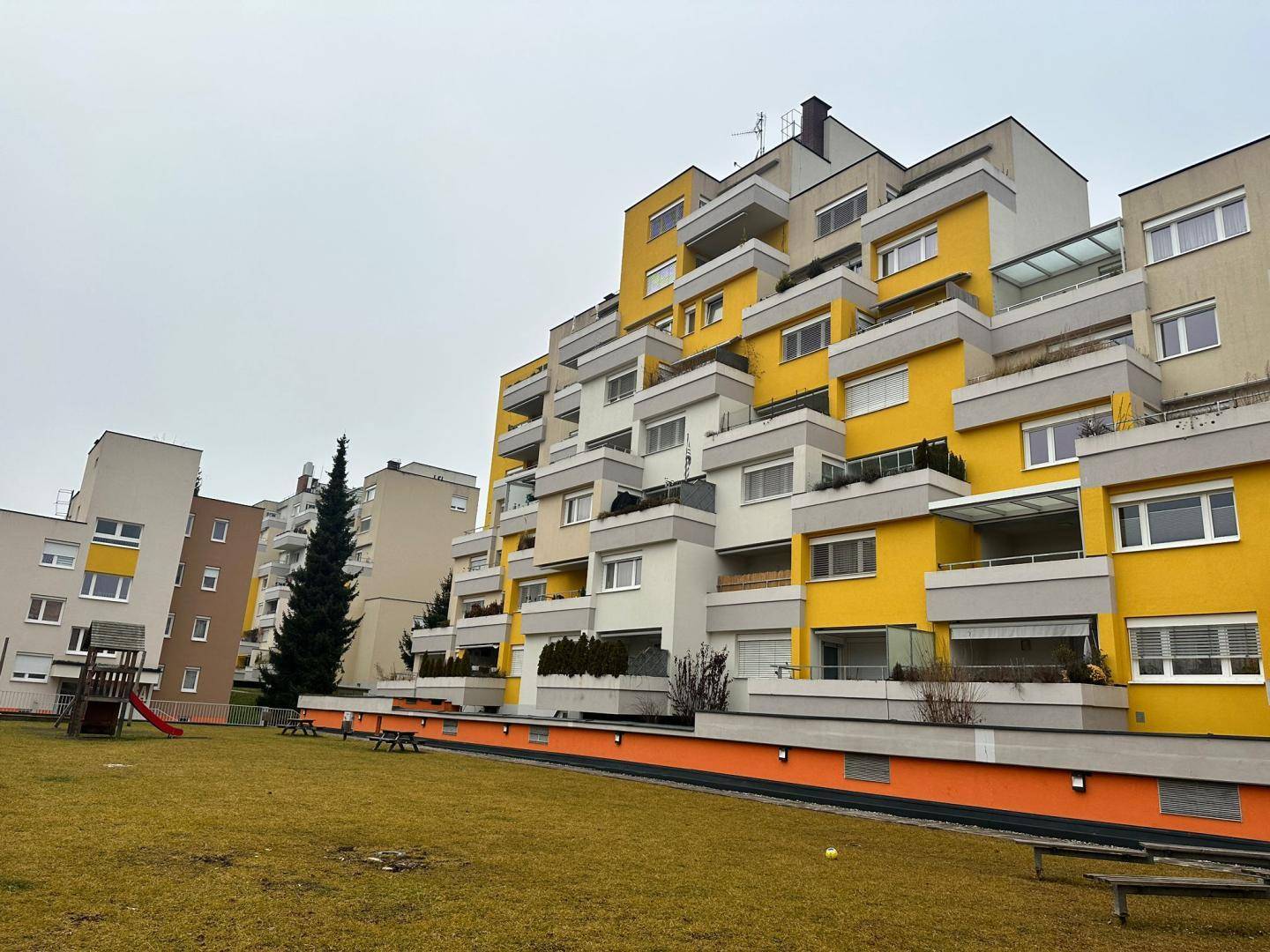 Modernes Wohngebäude mit gelben Fassadenakzenten, Balkonen und einem Spielplatz im Vordergrund.