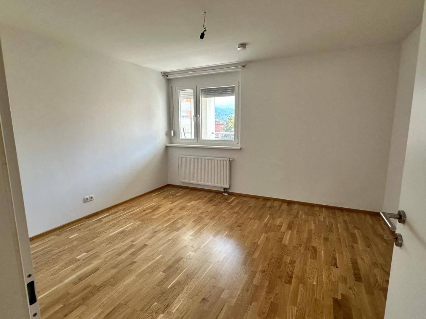 Helles Schlafzimmer mit Parkettboden und Fenster, das einen weiten Blick in die Landschaft bietet.