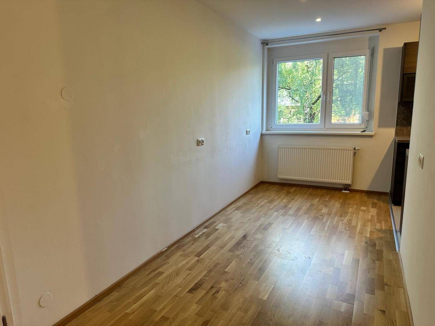Heller Raum mit Parkettboden und Fenster, das einen Blick ins Grüne bietet.