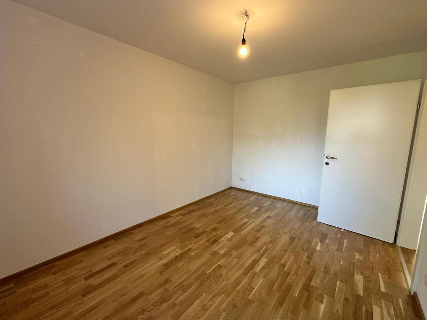 Leeres Schlafzimmer mit Parkettboden und weiß gestrichenen Wänden, bereit zur Einrichtung.