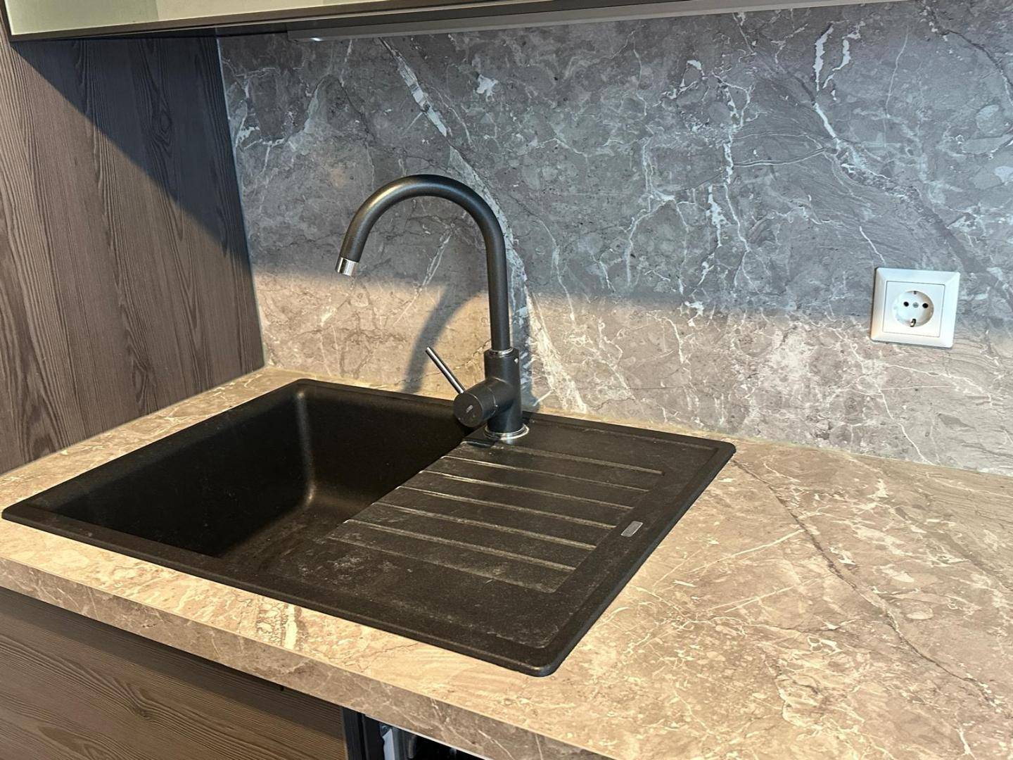 Detailaufnahme der Küchenspüle mit schwarzem Wasserhahn und passendem Spülbecken in Steinoptik-Arbeitsplatte.