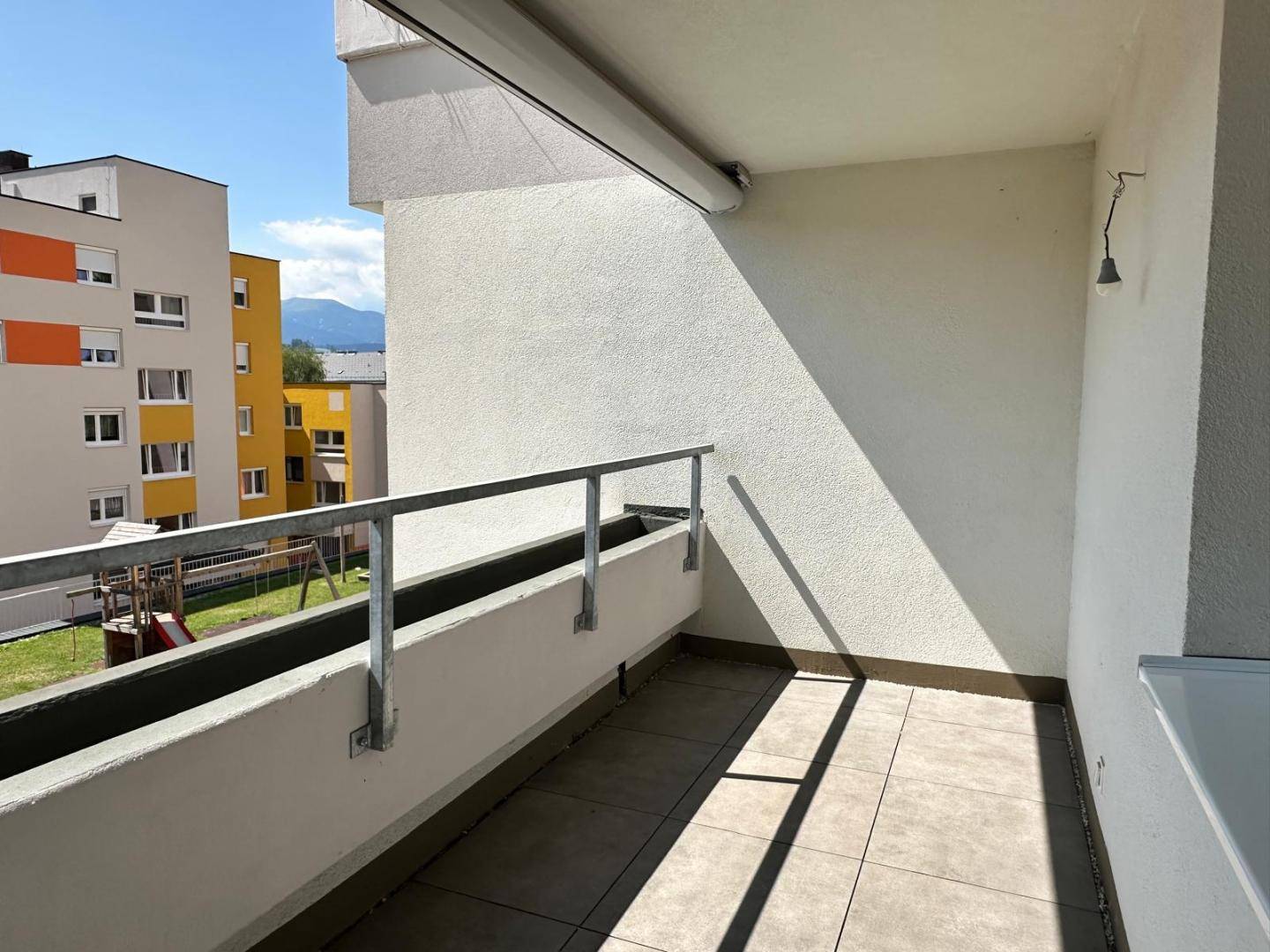 Sonnige Loggia mit Fliesenboden und Blick auf die umliegenden Gebäude und Berge.