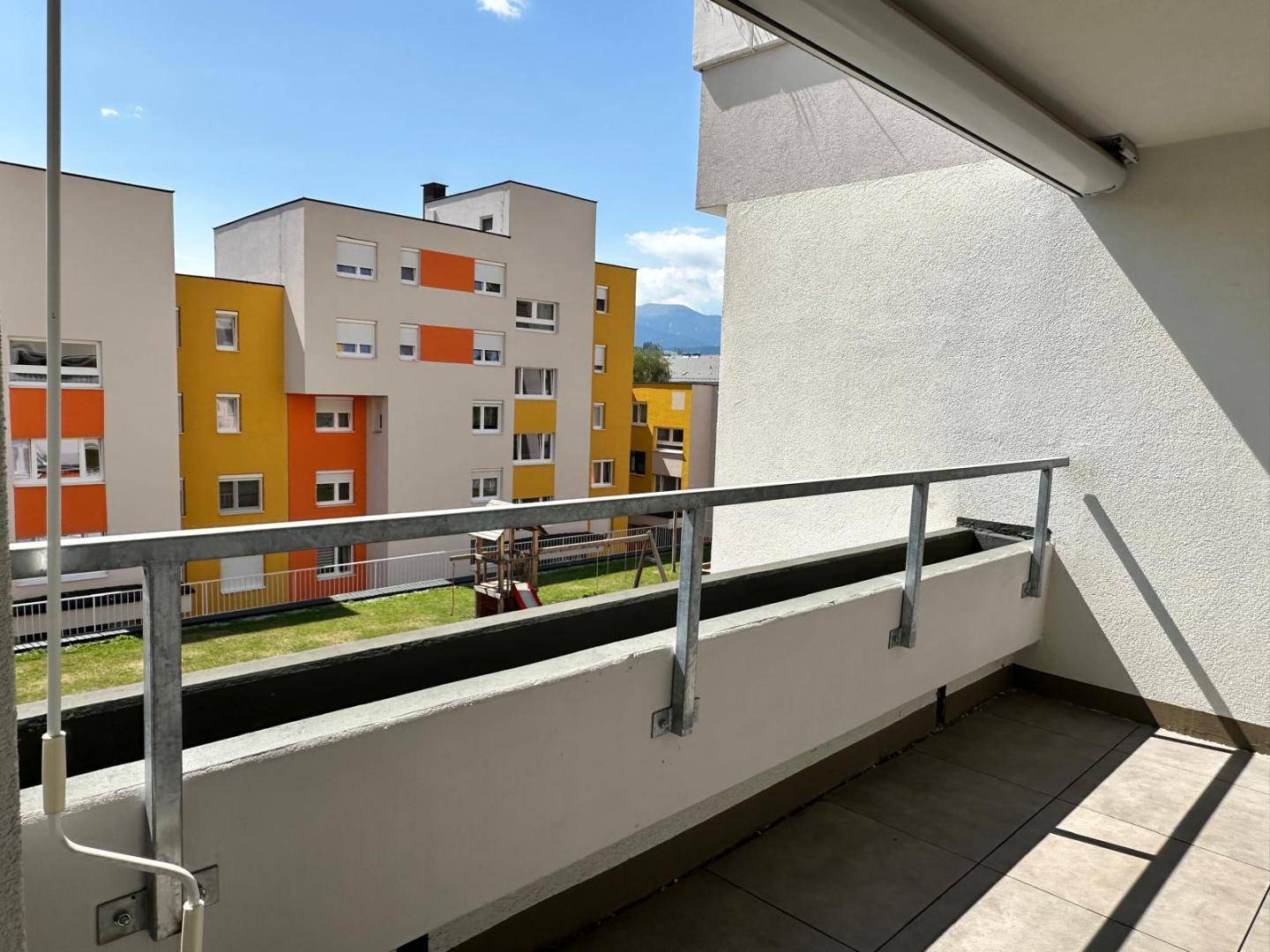 Sonnige Loggia mit Fliesenboden und Blick auf die umliegenden Gebäude und einen Spielplatz.
