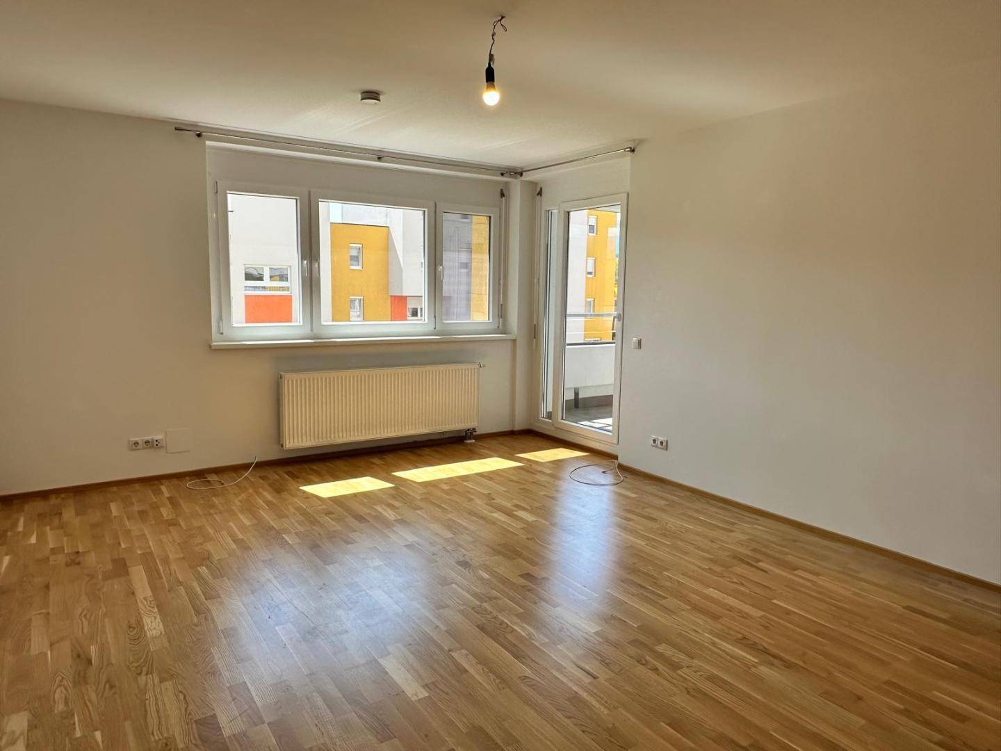 Geräumiges Wohnzimmer mit Parkettboden, großen Fenstern und Zugang zum Balkon.