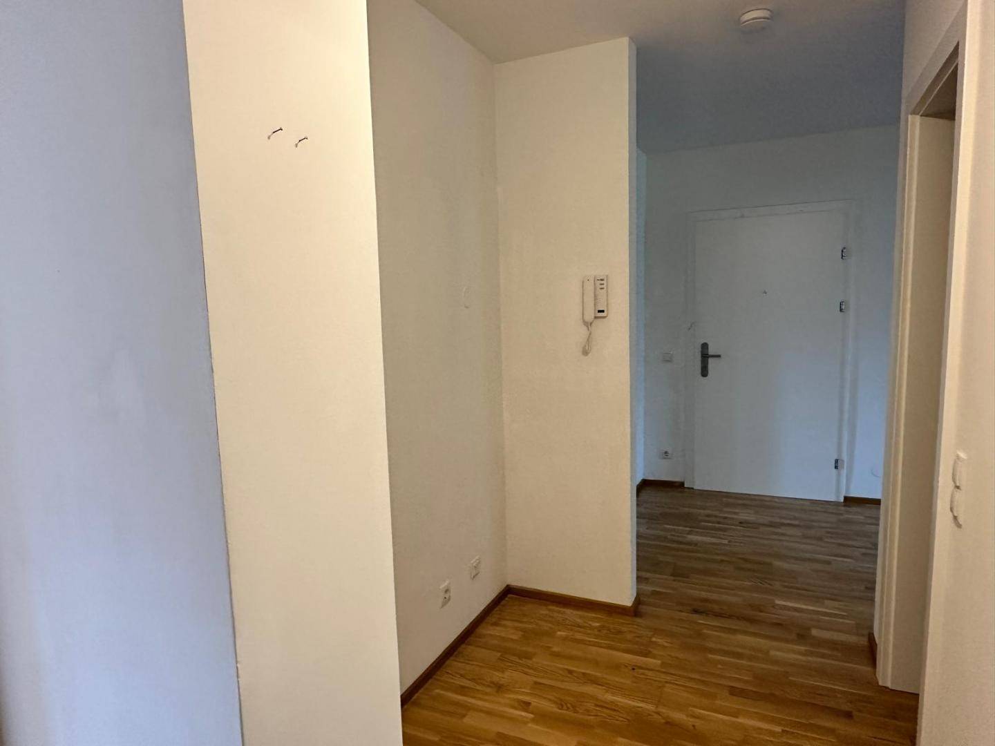 Heller Flur mit Parkettboden und Gegensprechanlage, der zu weiteren Räumen führt.