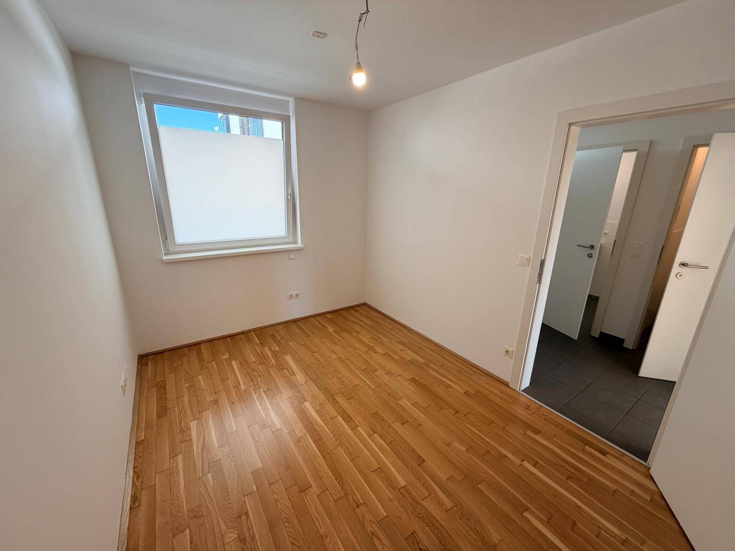 Schlafzimmer mit Holzboden und Zugang zu einem weiteren Raum, ideal als Gästezimmer.