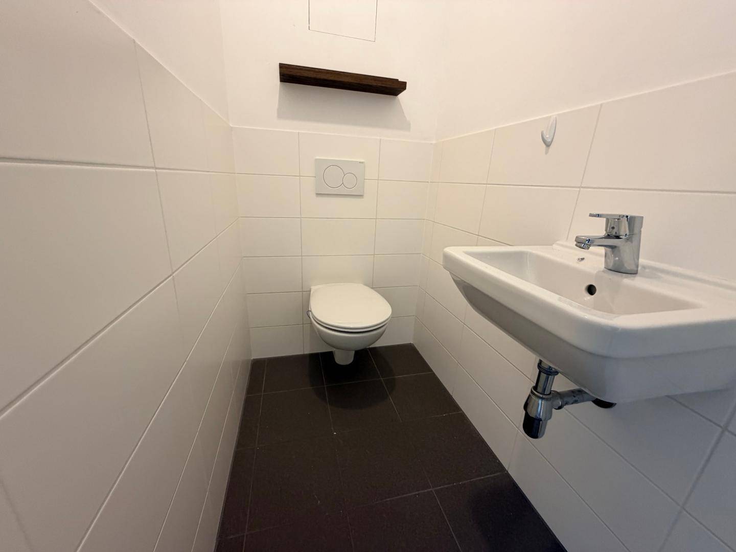 Modernes Gäste-WC mit Wand-WC, kleinem Waschbecken und weißen Fliesen.