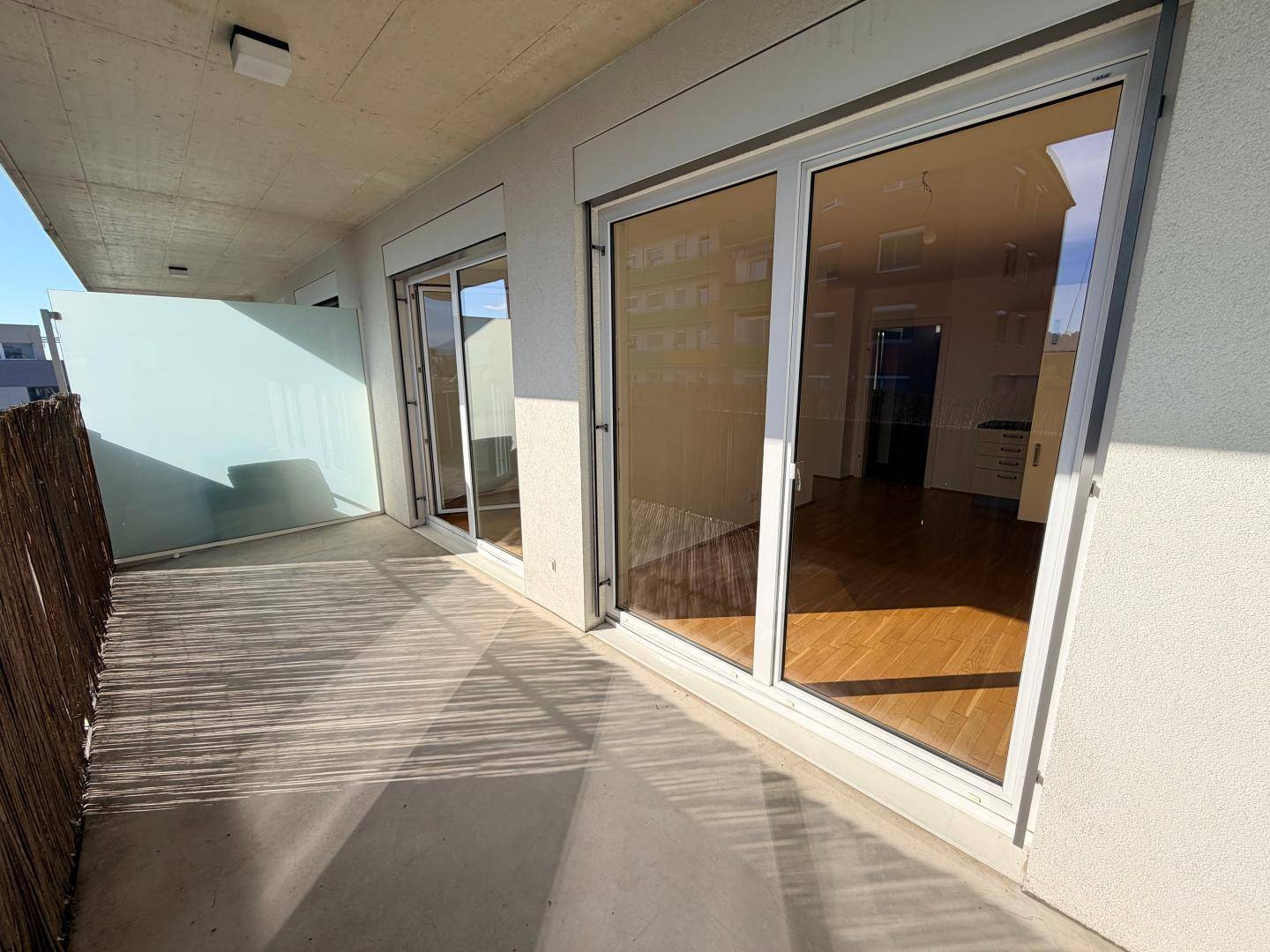 Sonniger Balkon mit Schiebetüren zum Innenbereich und einer Sichtschutzwand.