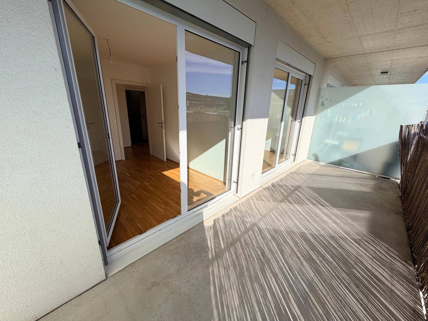 Geräumiger Balkon mit Betonboden und Blick auf die Umgebung, ideal zum Entspannen.