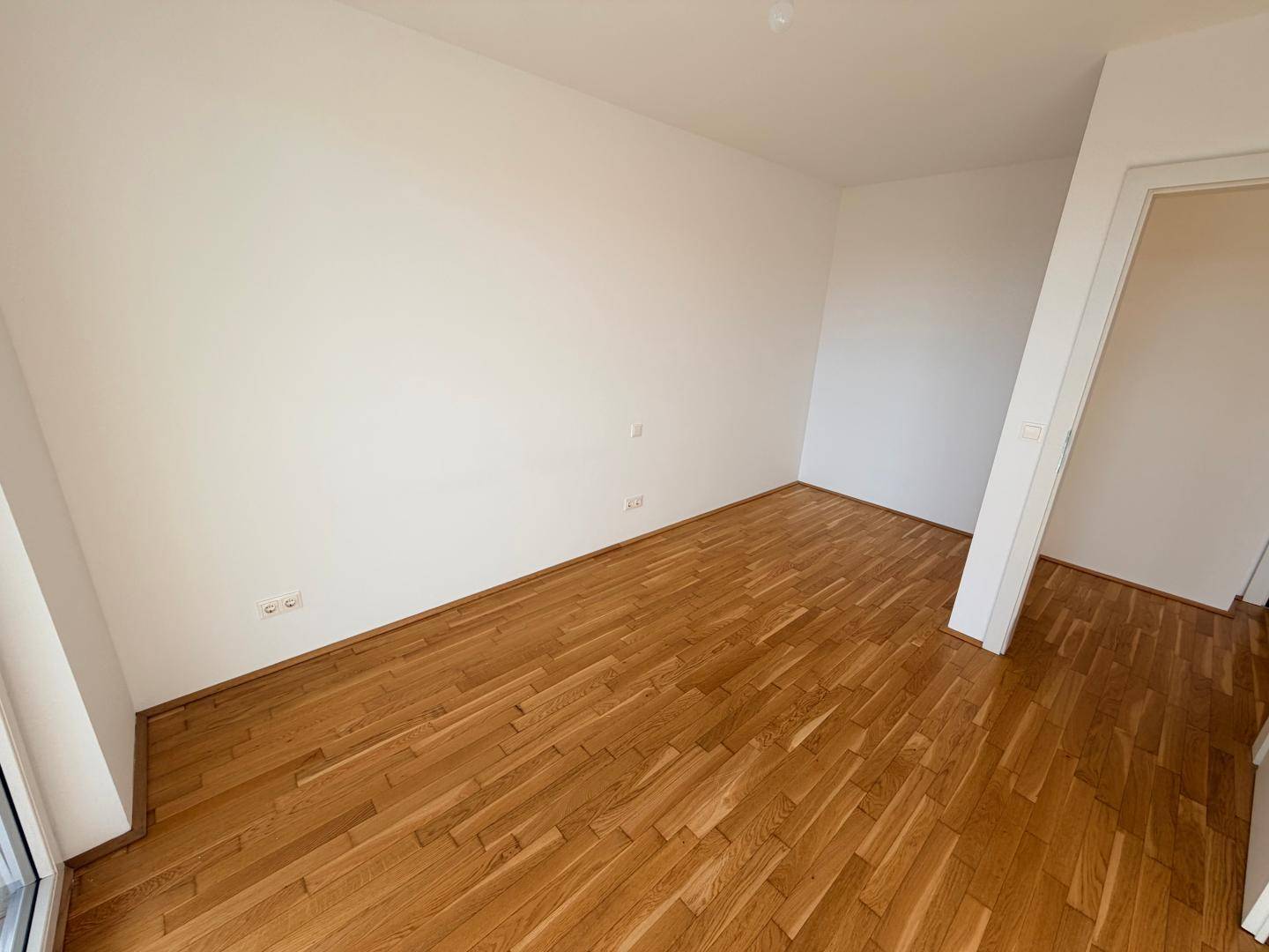 Leerer Wohnraum mit Parkettboden und weißen Wänden, bereit für individuelle Gestaltung.