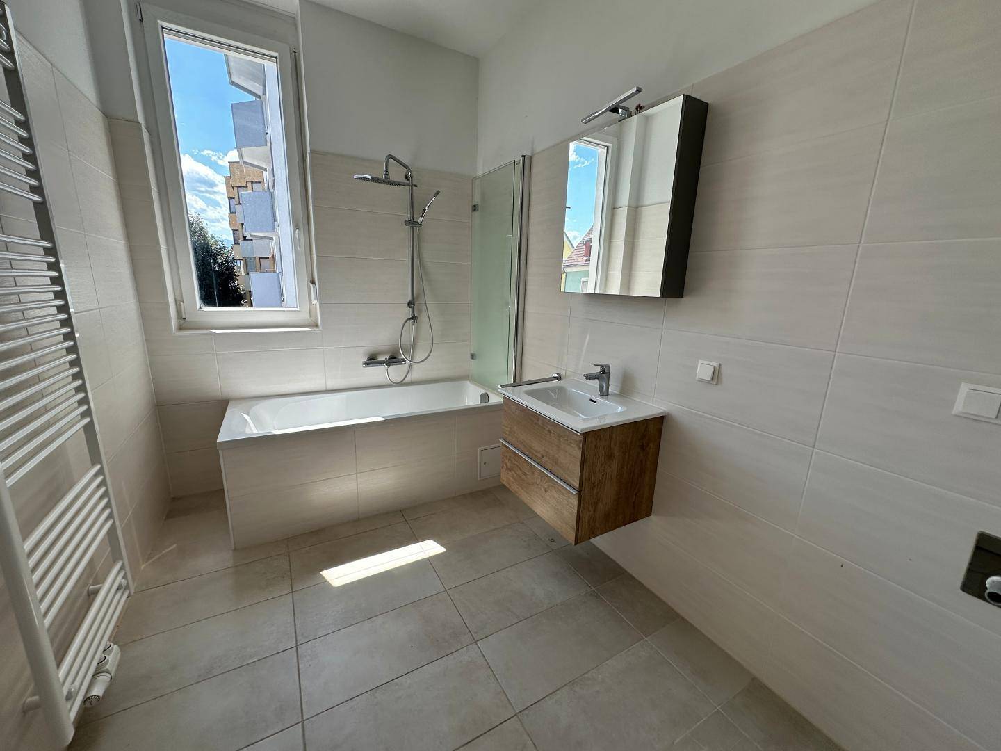 Modernes Badezimmer mit Badewanne, Dusche, Waschbecken und beheiztem Handtuchhalter.